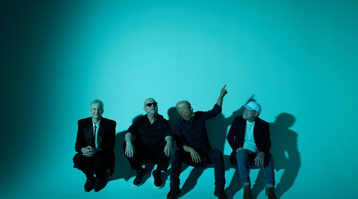 Members of the band the pixies sitting on the floor of a studio with blue lighting